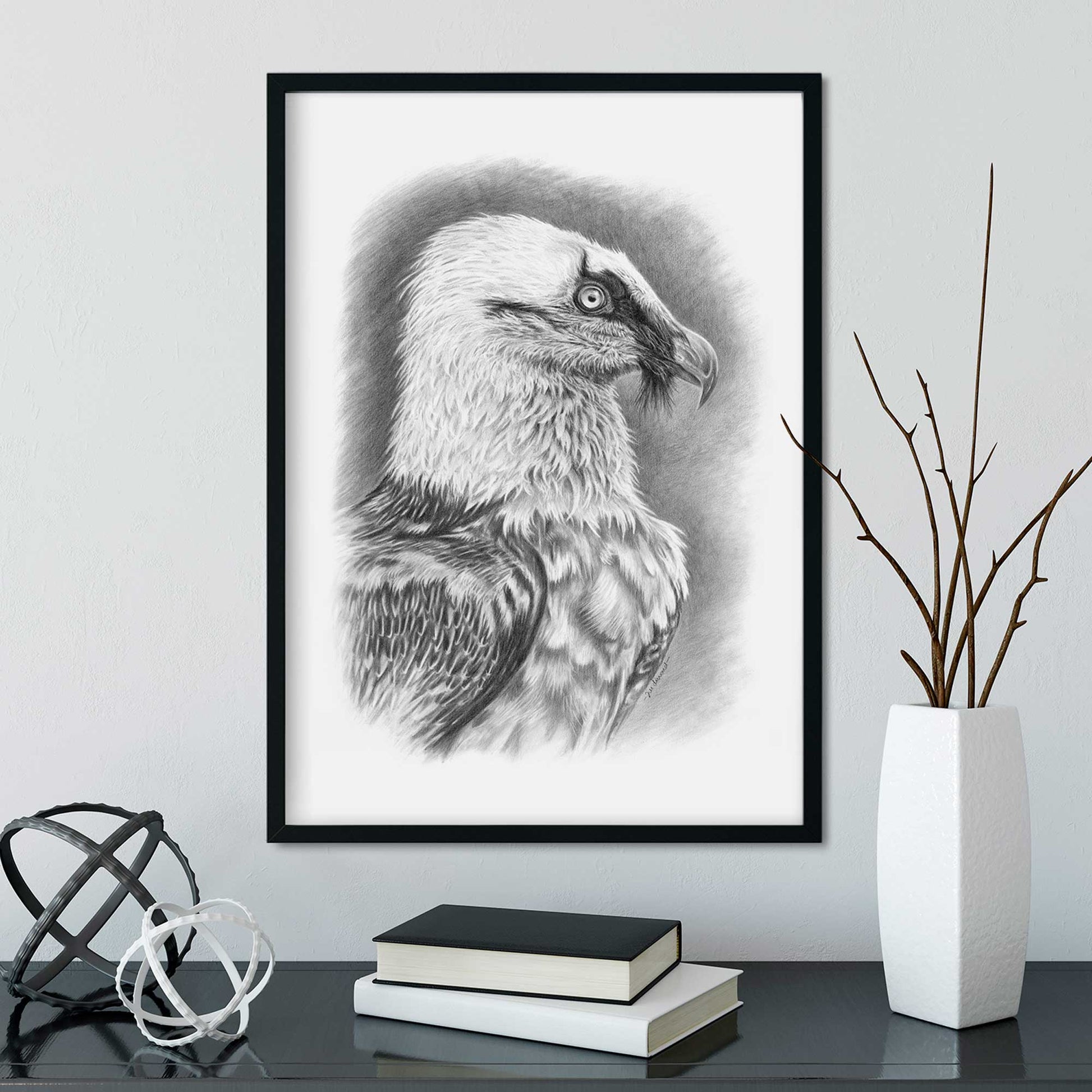 Black frame on wall with black and white picture of vulture bird, desk below with ornaments and books