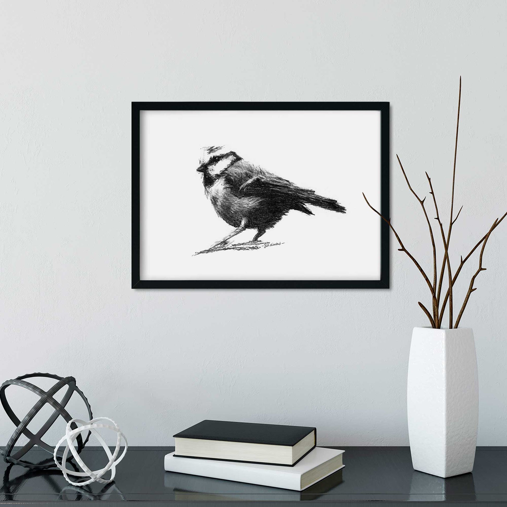 Bird drawing in a frame on a grey wall with vase and books below