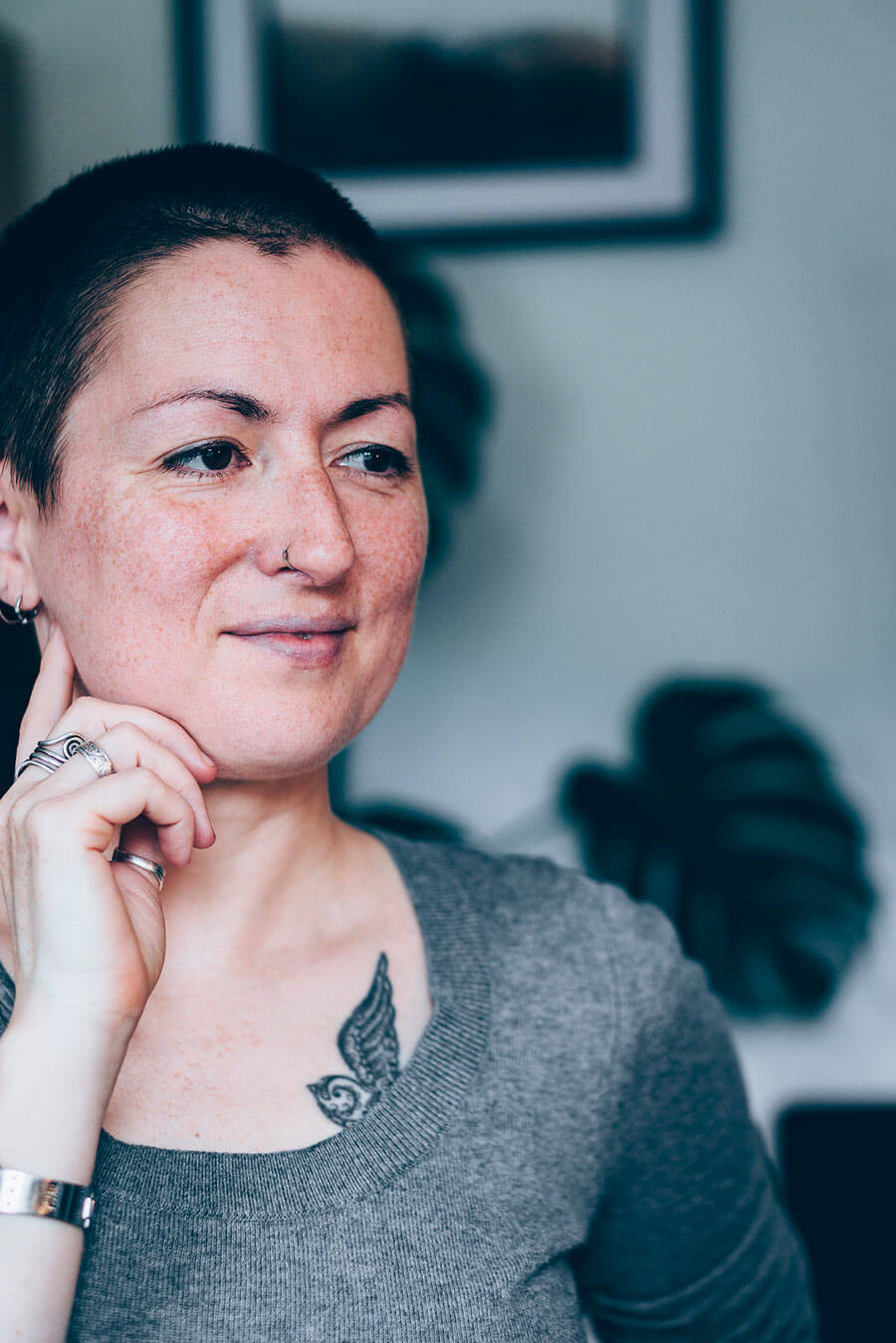 Portrait of Jill Dimond, bird artist, looking out to the right with herh and up to the side of her face. There are white walls behind and the outline of a plant.