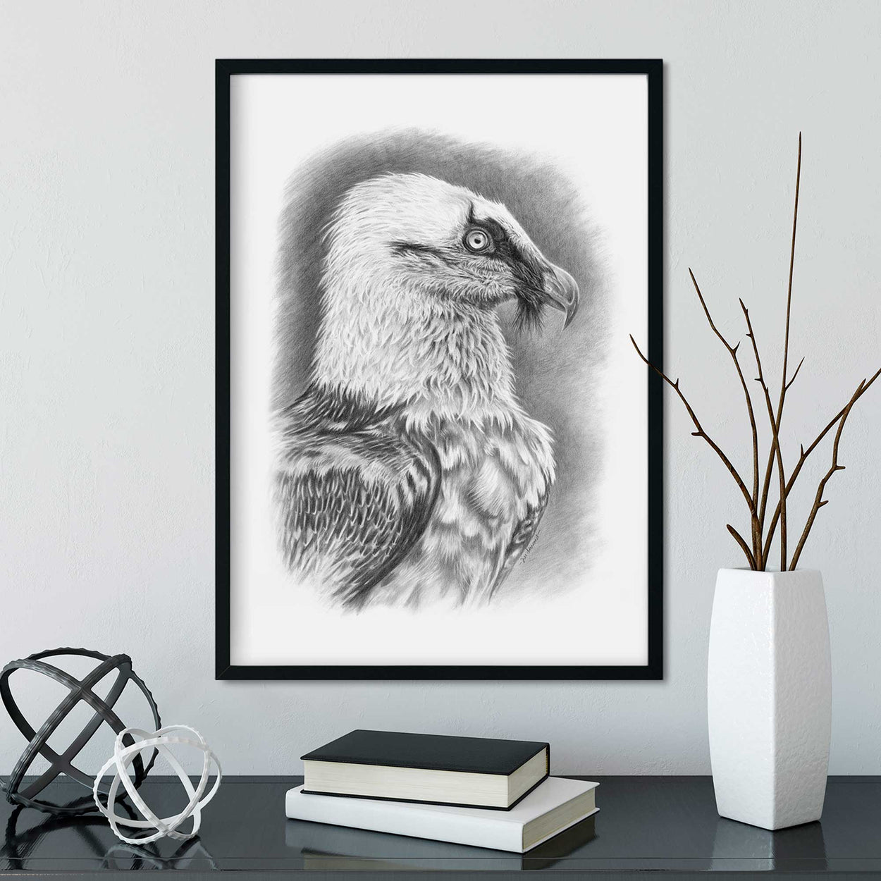 Black frame on wall with black and white picture of vulture bird, desk below with ornaments and books