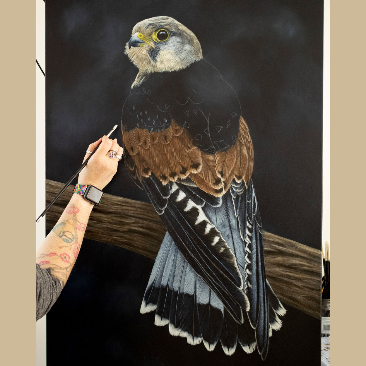 Imaging showing an arm holding a paintbrush over a part-completed painting of a male common kestrel