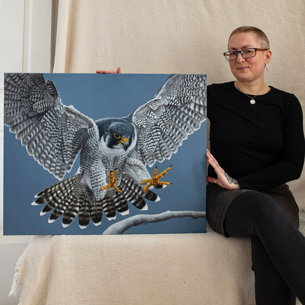 Bird of prey artist Jill Dimond sitting next to the original painting of a flying peregrine