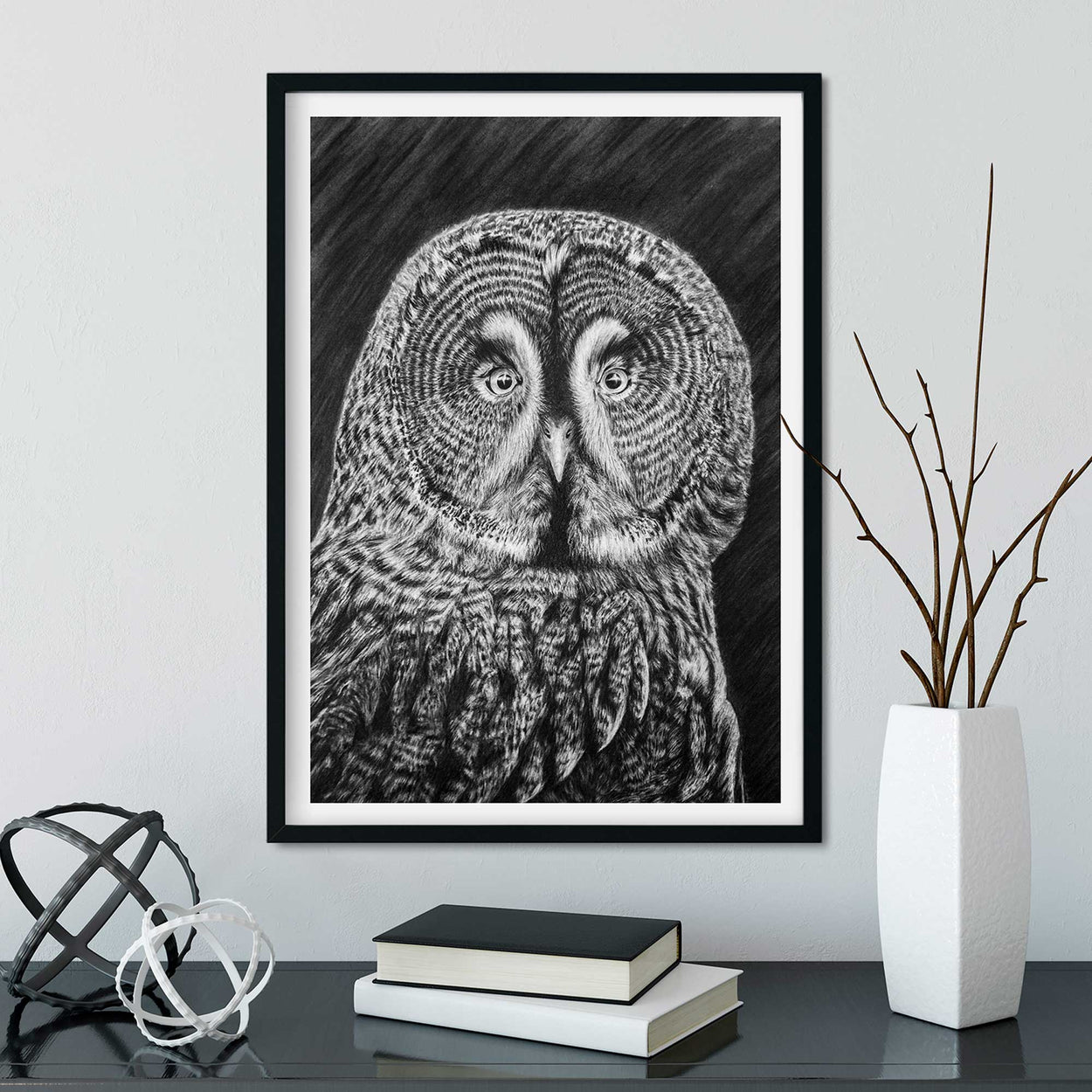 Frame on wall containing black and white drawing of a great grey owl.  Desk below with books and ornaments on it