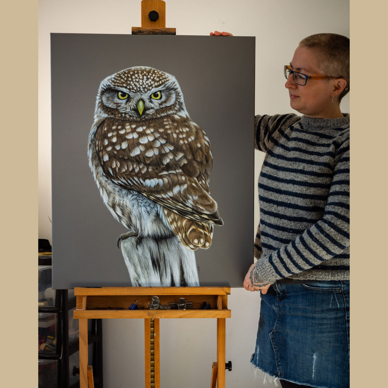 Bird artist Jill Dimond stood next to a little owl painting on a wooden easel