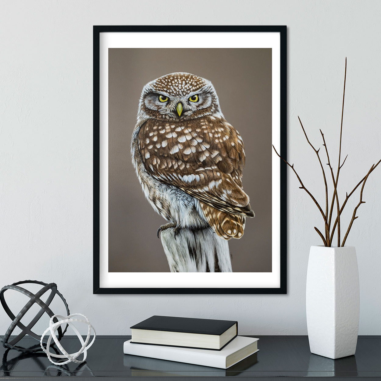 Painting of a little owl in a black frame on a white wall