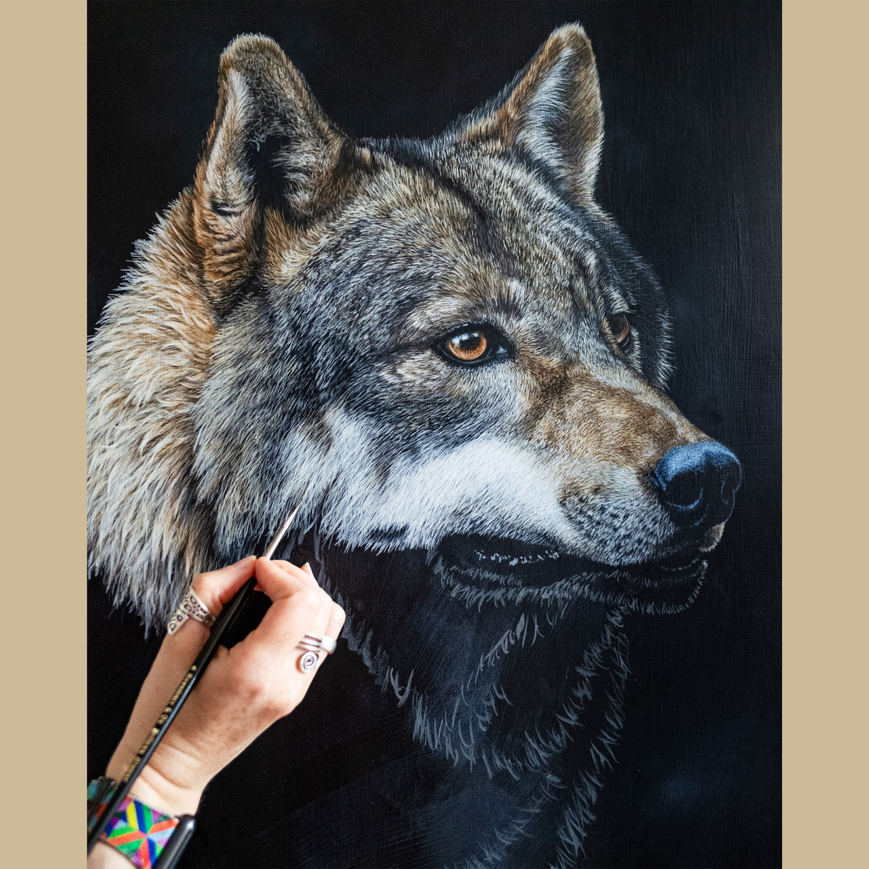 A hand holding a brush over the part-completed painting of a wolf face
