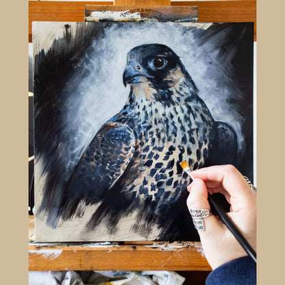 Painting of a peregrine falcon on an easel with a hand holding a paintbrush by Jill Dimond