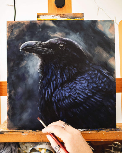 Raven painting work in progress on an easel with the artist's hand holding a paintbrush, by bird artist Jill Dimond.